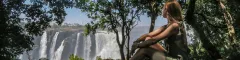 Young woman sitting on a rock in the rain forest and looking at victoria falls